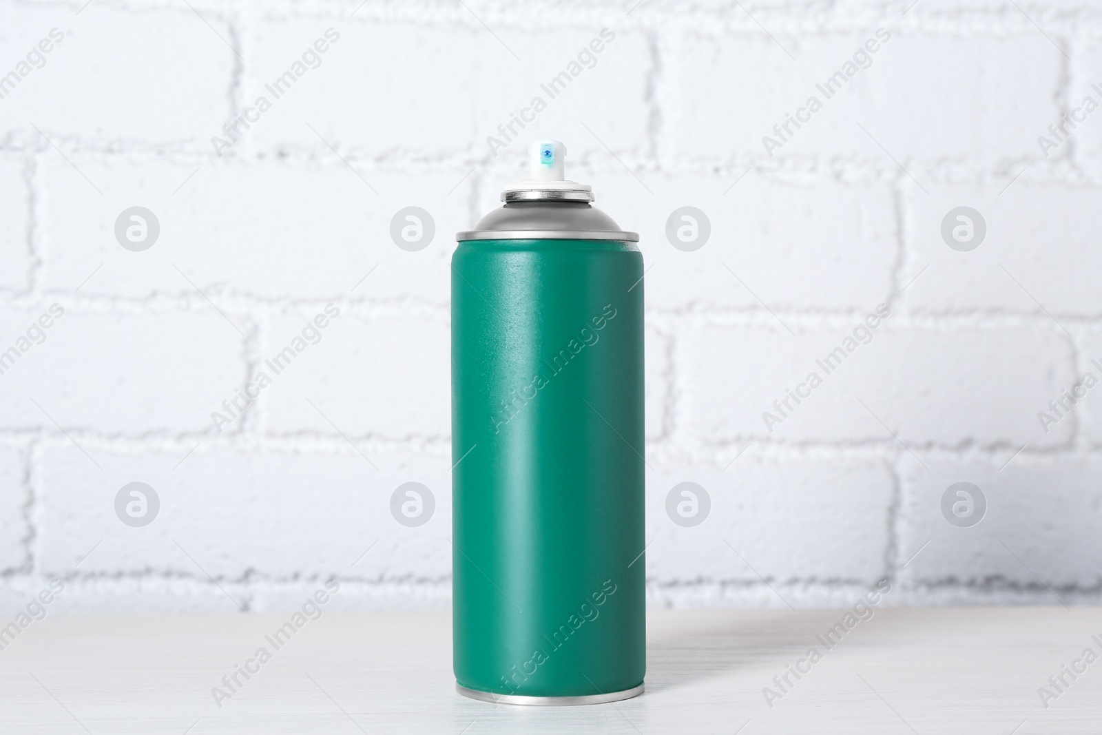 Photo of Can of spray paint on wooden table near white brick wall