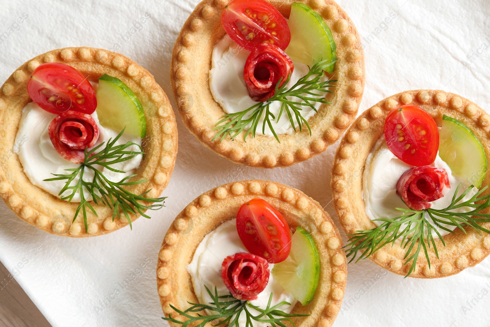 Photo of Delicious canapes with dry smoked sausages, cream cheese and vegetables on table, flat lay