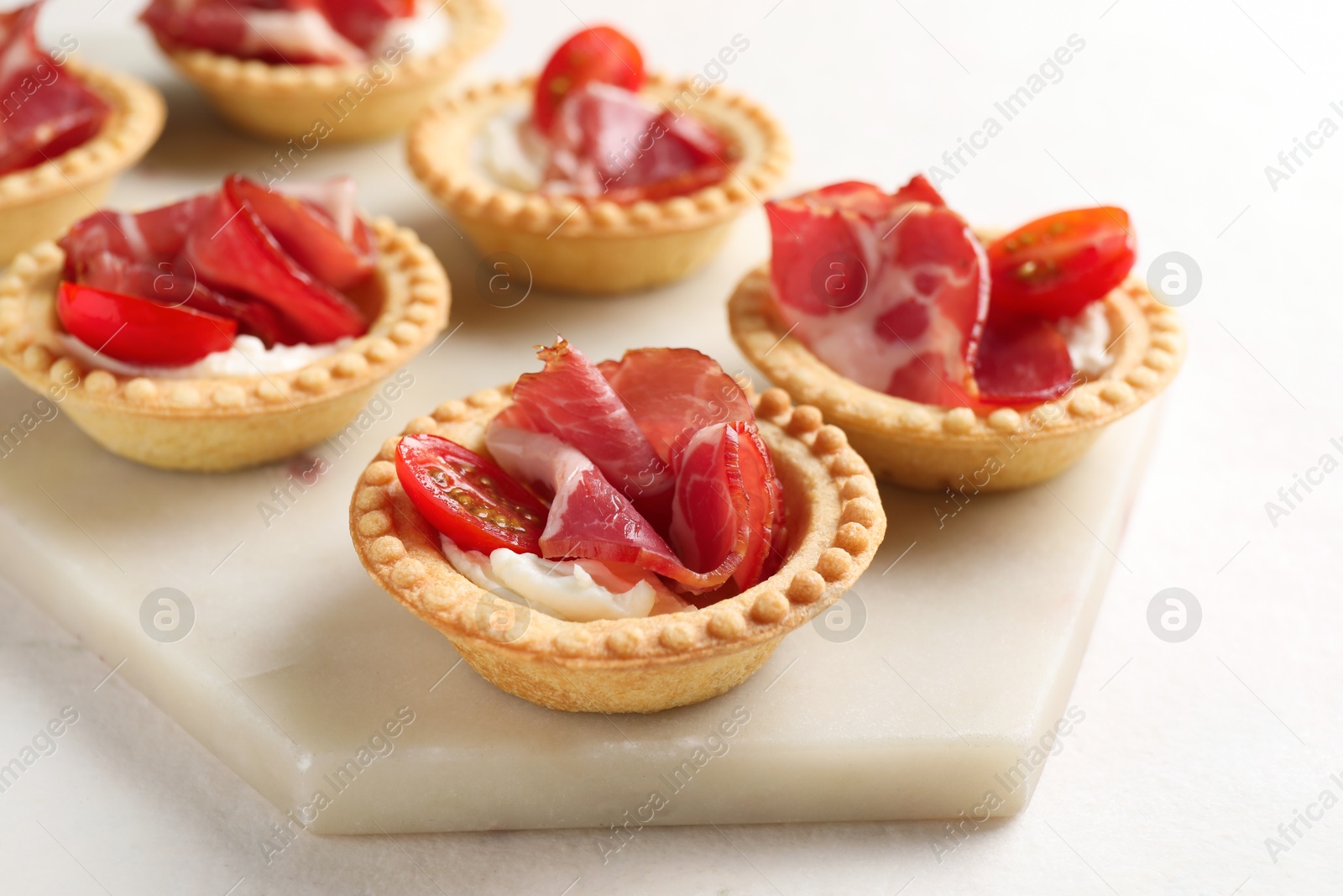 Photo of Delicious canapes with jamon, cream cheese and cherry tomatoes on light table, closeup