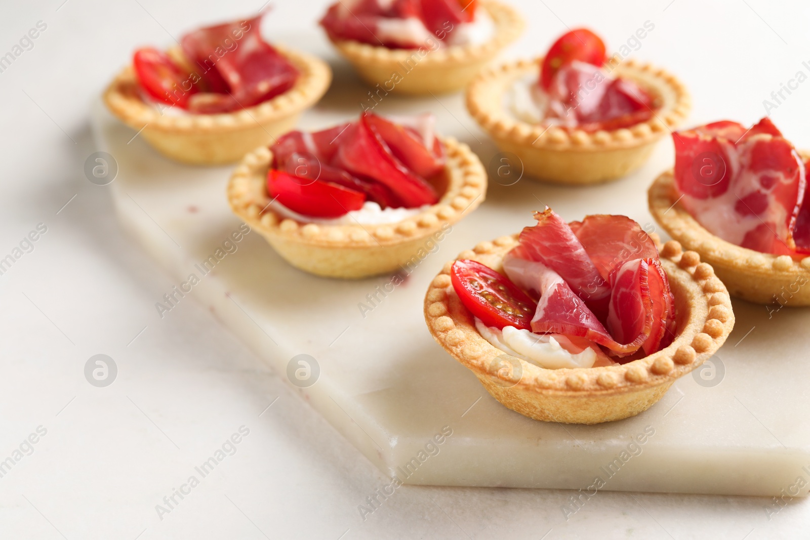 Photo of Delicious canapes with jamon, cream cheese and cherry tomatoes on light table, closeup