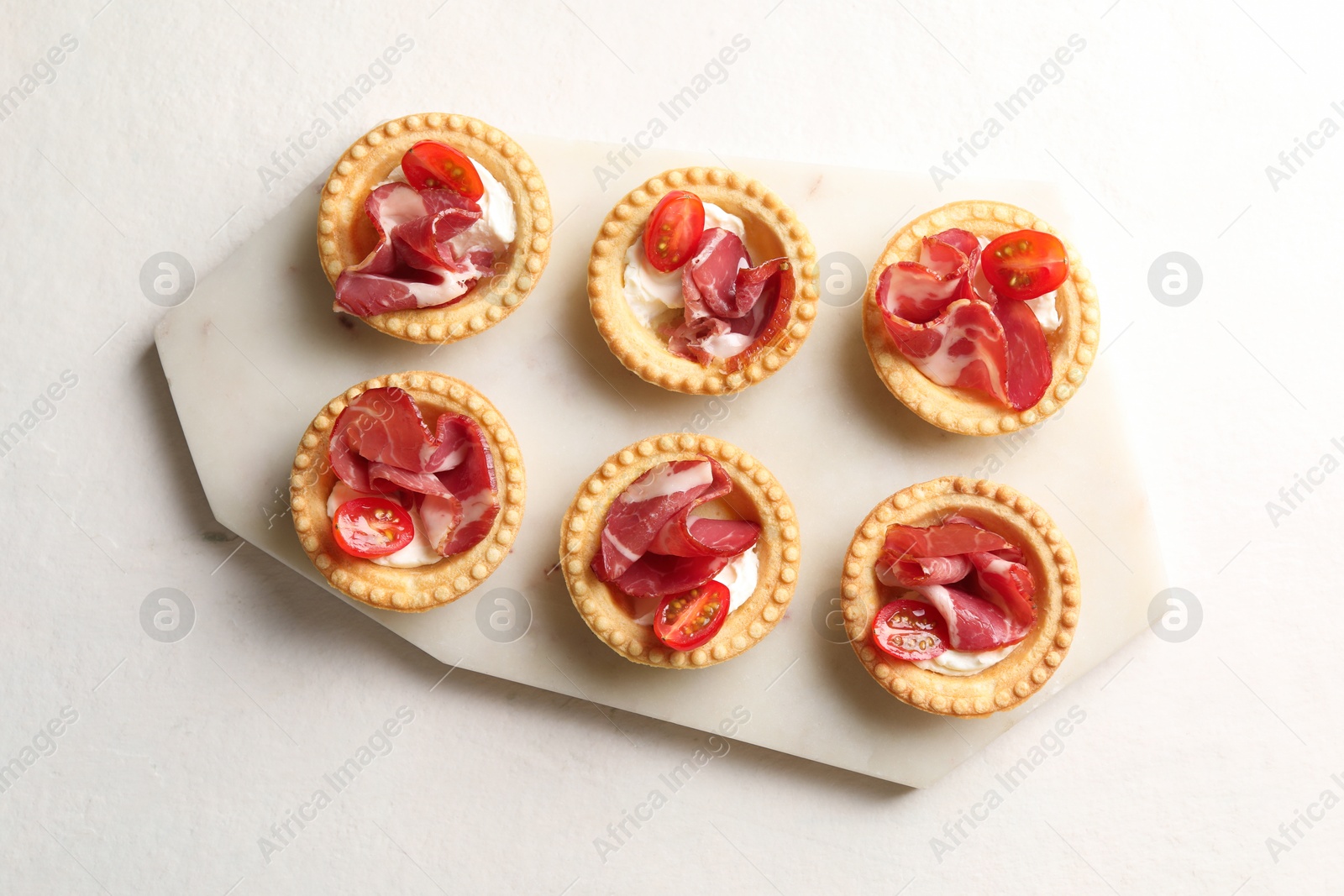 Photo of Delicious canapes with jamon, cream cheese and cherry tomatoes on white table, top view