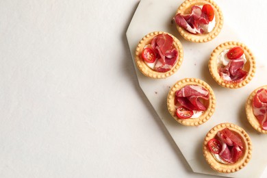 Photo of Delicious canapes with jamon, cream cheese and cherry tomatoes on light table, top view. Space for text