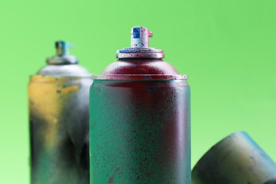 Photo of Bright spray paint cans on green background, closeup