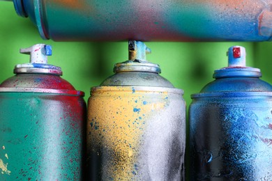 Many spray paint cans on green background, flat lay