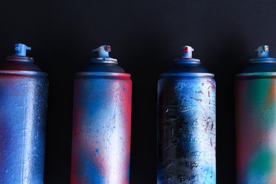 Many spray paint cans on dark background, flat lay