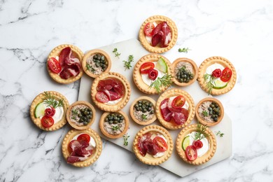 Different delicious canapes on white marble table, flat lay