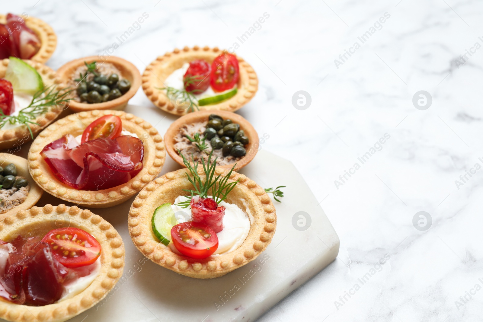 Photo of Different delicious canapes on white marble table, space for text