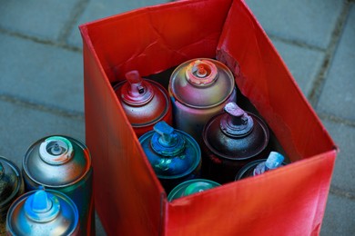 Many spray paint cans and red cardboard box outdoors, closeup