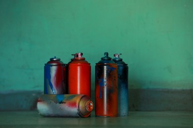 Many spray paint cans near green wall