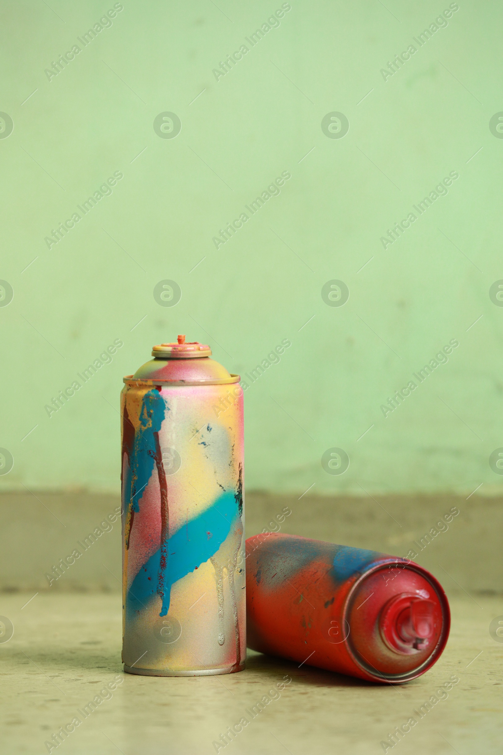 Photo of Two spray paint cans against light green wall