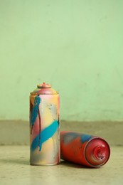 Photo of Two spray paint cans against light green wall