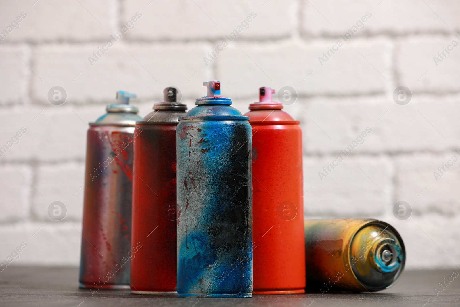 Photo of Many spray paint cans on gray surface against white brick wall