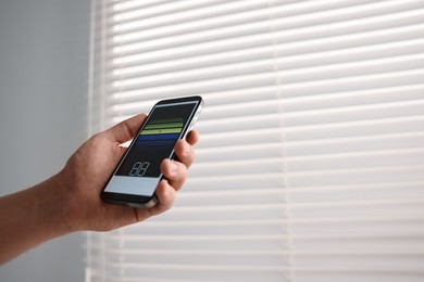 Man using phone to adjust window blinds indoors, closeup. Space for text