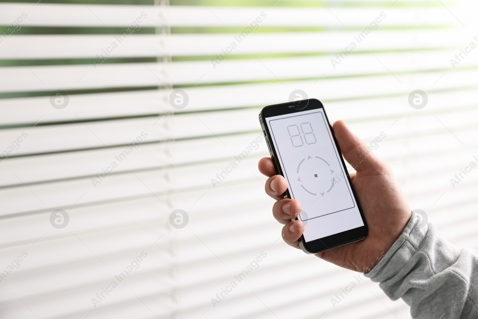 Photo of Man using phone to adjust window blinds indoors, closeup. Space for text