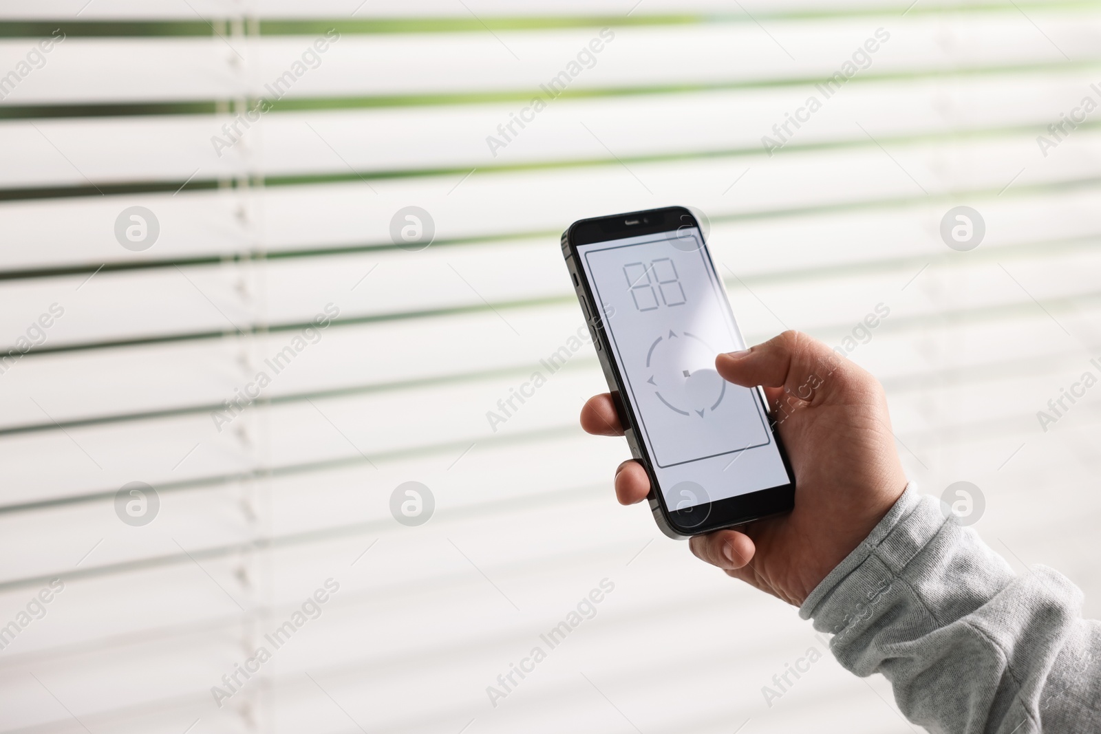 Photo of Man using phone to adjust window blinds indoors, closeup. Space for text