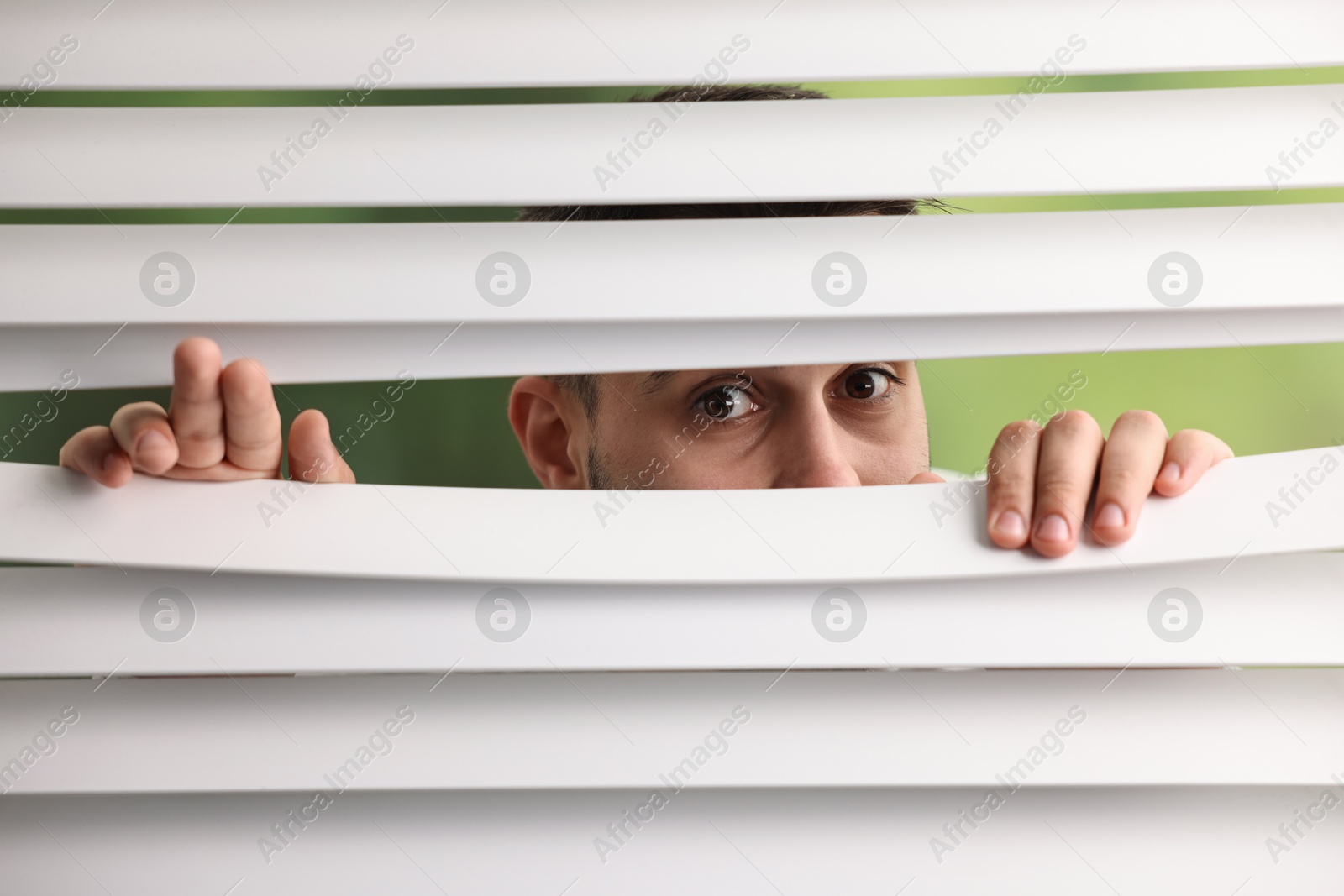 Photo of Young man looking through window blinds on blurred background