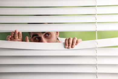 Photo of Young man looking through window blinds on blurred background