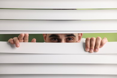 Photo of Young man looking through window blinds on blurred background