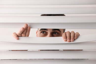 Young man looking through window blinds on white background