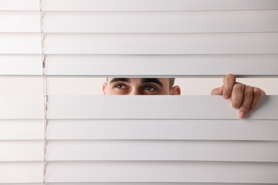 Young man looking through window blinds on white background