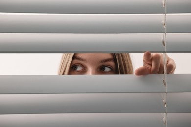 Young woman looking through window blinds on white background