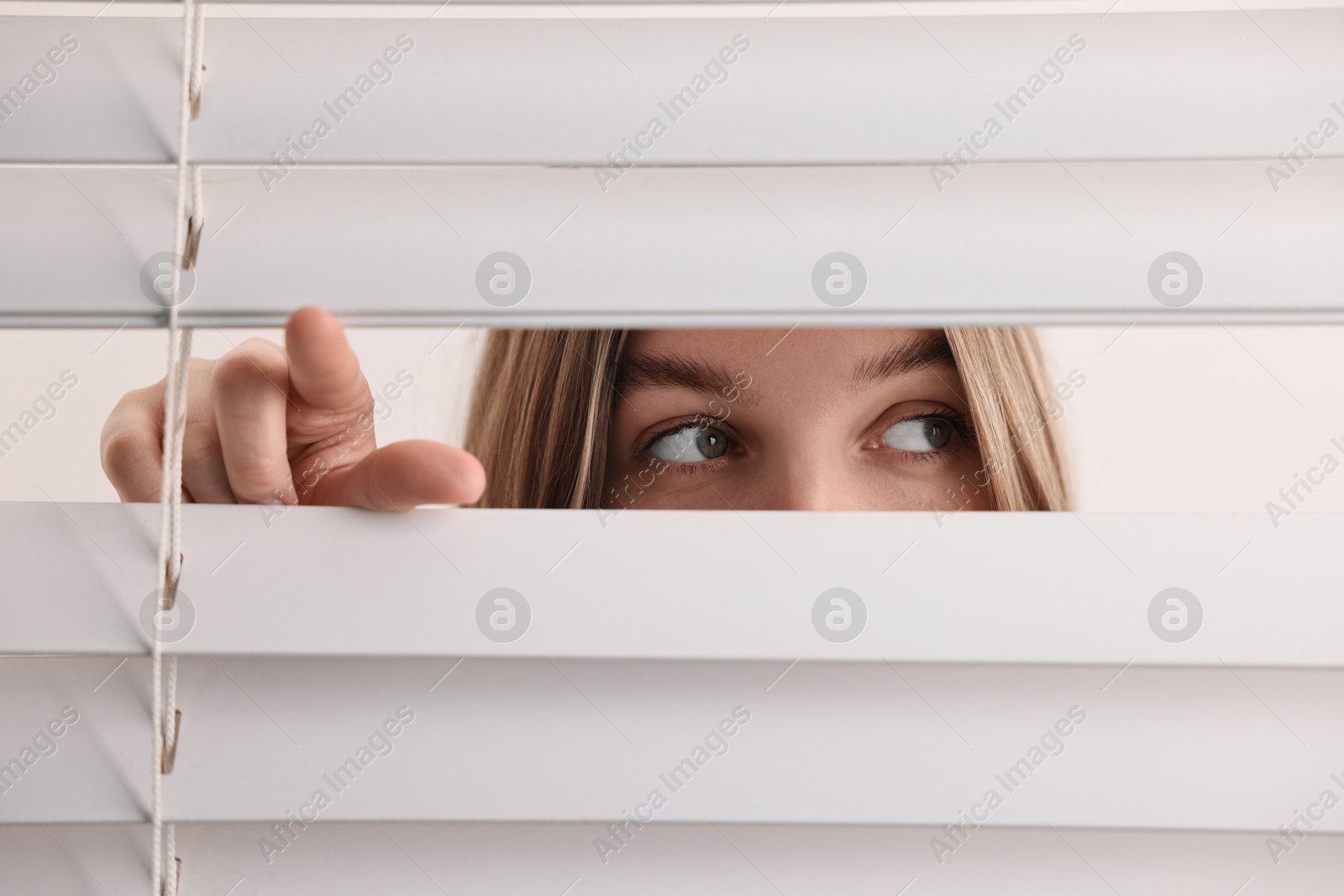 Photo of Young woman looking through window blinds on white background