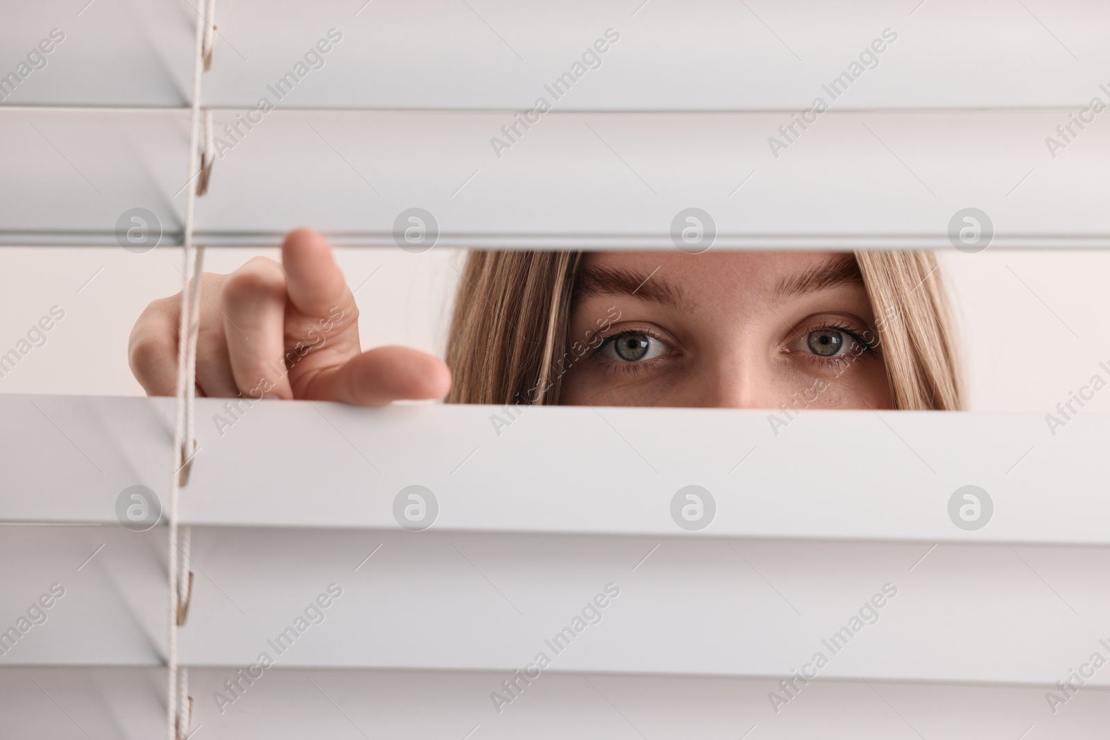 Photo of Young woman looking through window blinds on white background