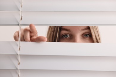 Young woman looking through window blinds on white background