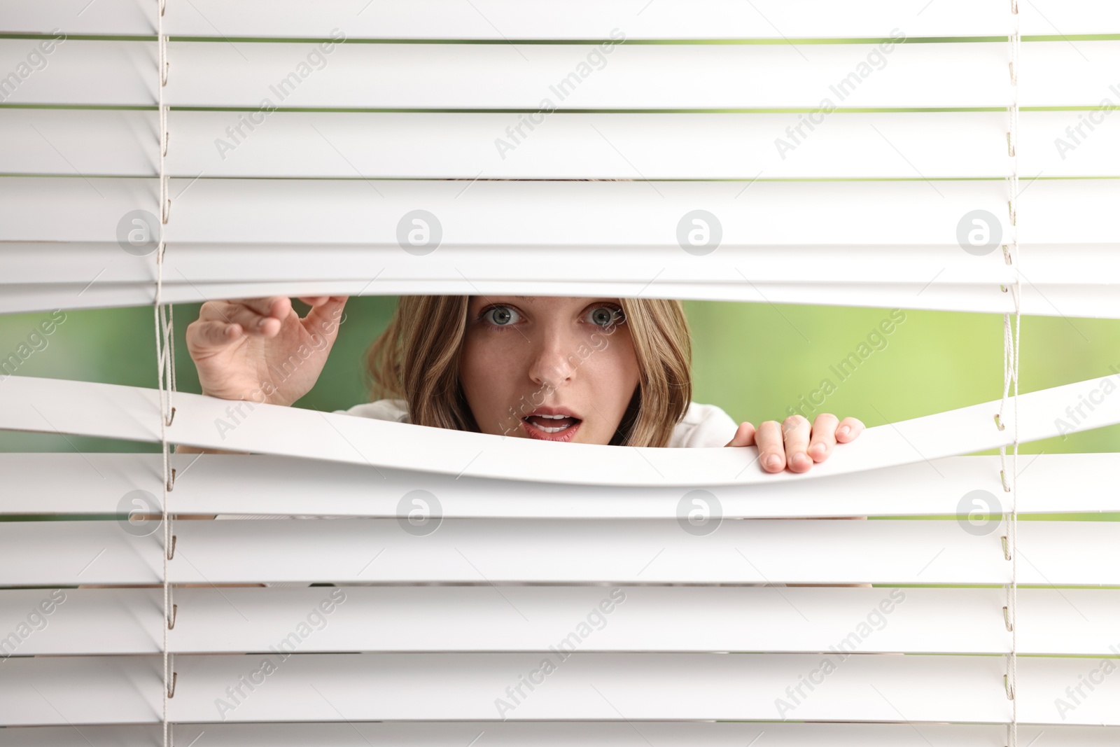 Photo of Young woman looking through window blinds on blurred background