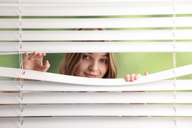 Young woman looking through window blinds on blurred background