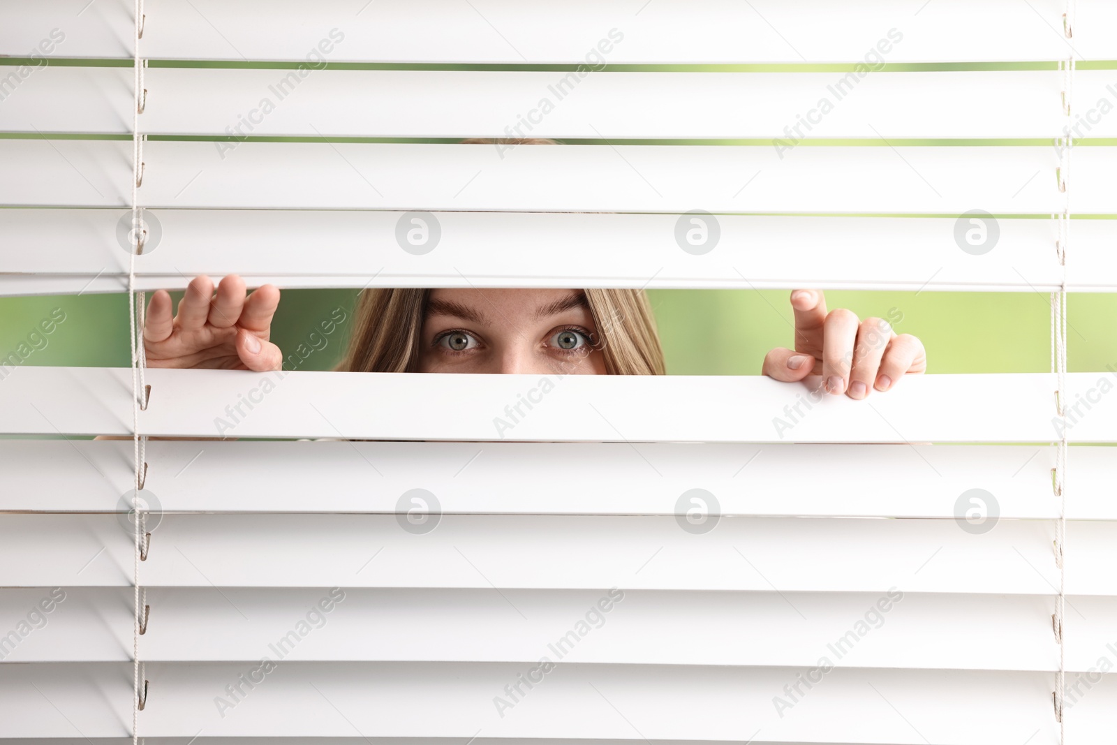 Photo of Young woman looking through window blinds on blurred background