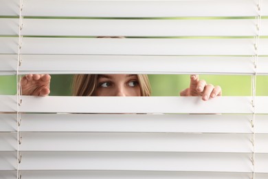 Photo of Young woman looking through window blinds on blurred background