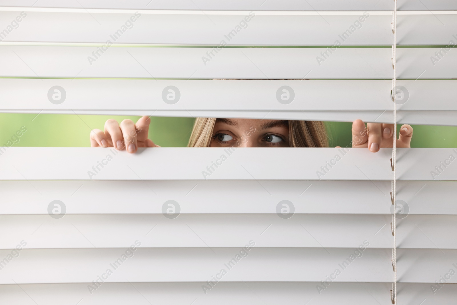 Photo of Young woman looking through window blinds on blurred background