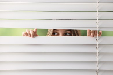 Young woman looking through window blinds on blurred background