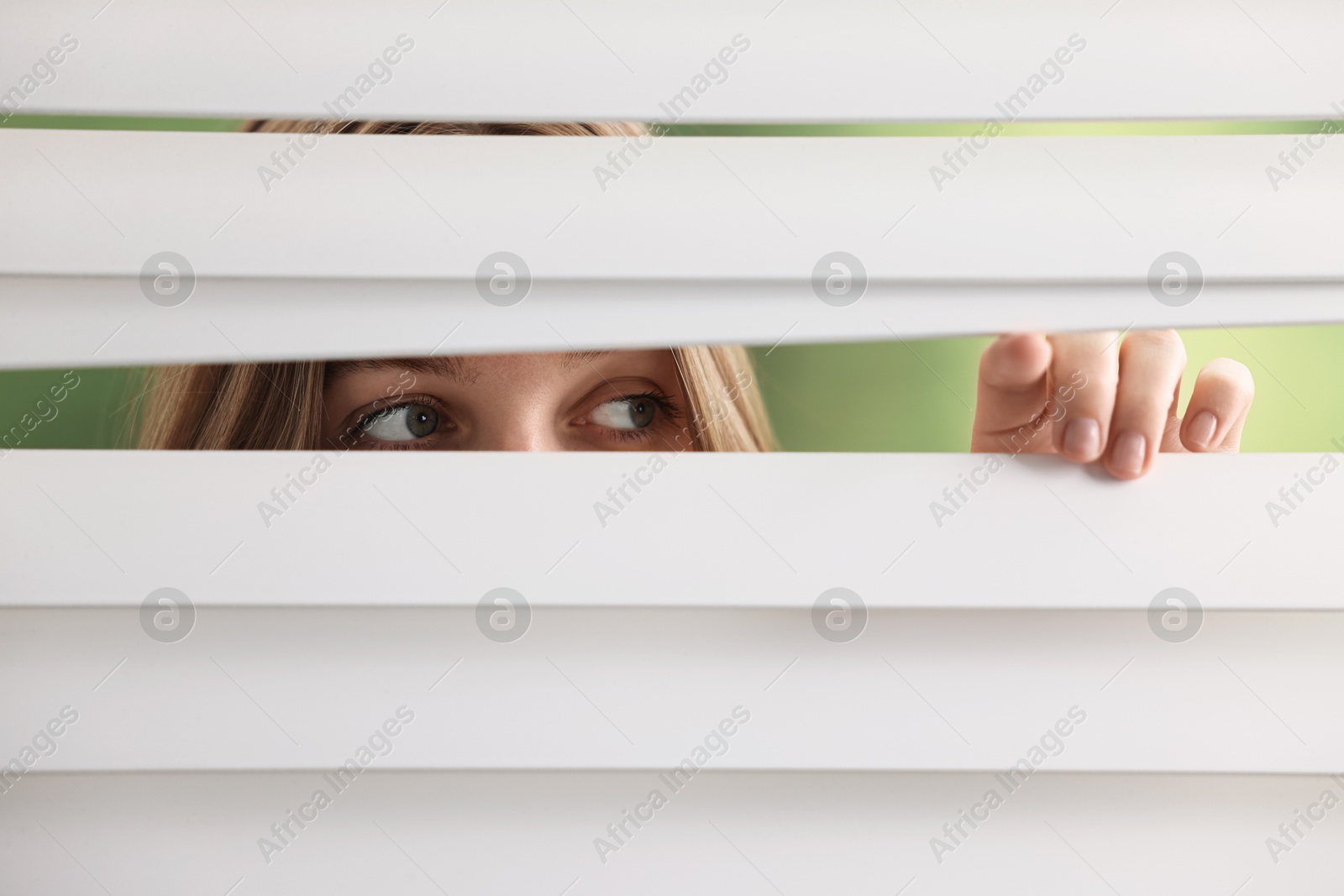 Photo of Young woman looking through window blinds on blurred background