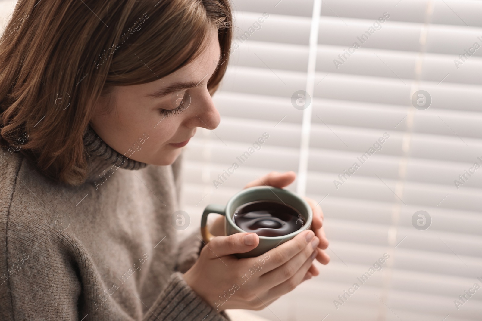 Photo of Woman with cup of drink near window blinds indoors, space for text