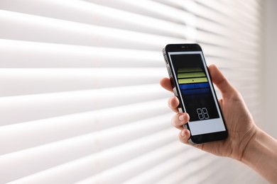 Woman using smartphone to adjust window blinds indoors, closeup. Space for text