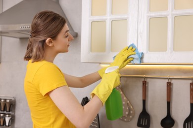 Professional janitor wearing uniform cleaning cabinet in kitchen