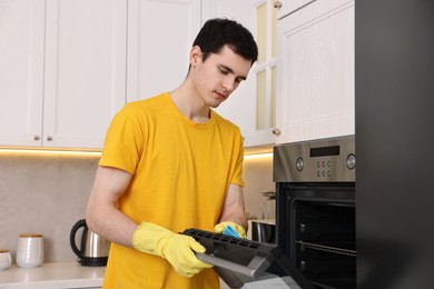 Photo of Professional janitor wearing uniform cleaning electric oven in kitchen