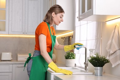 Professional janitor wearing uniform cleaning tap in kitchen