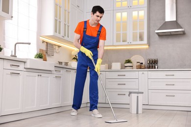 Photo of Cleaning service worker washing floor with mop in kitchen