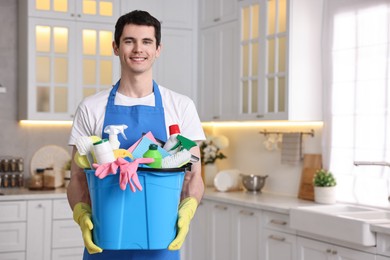 Photo of Cleaning service worker holding bucket with supplies in kitchen. Space for text