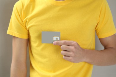 Man holding SIM card on grey background, closeup