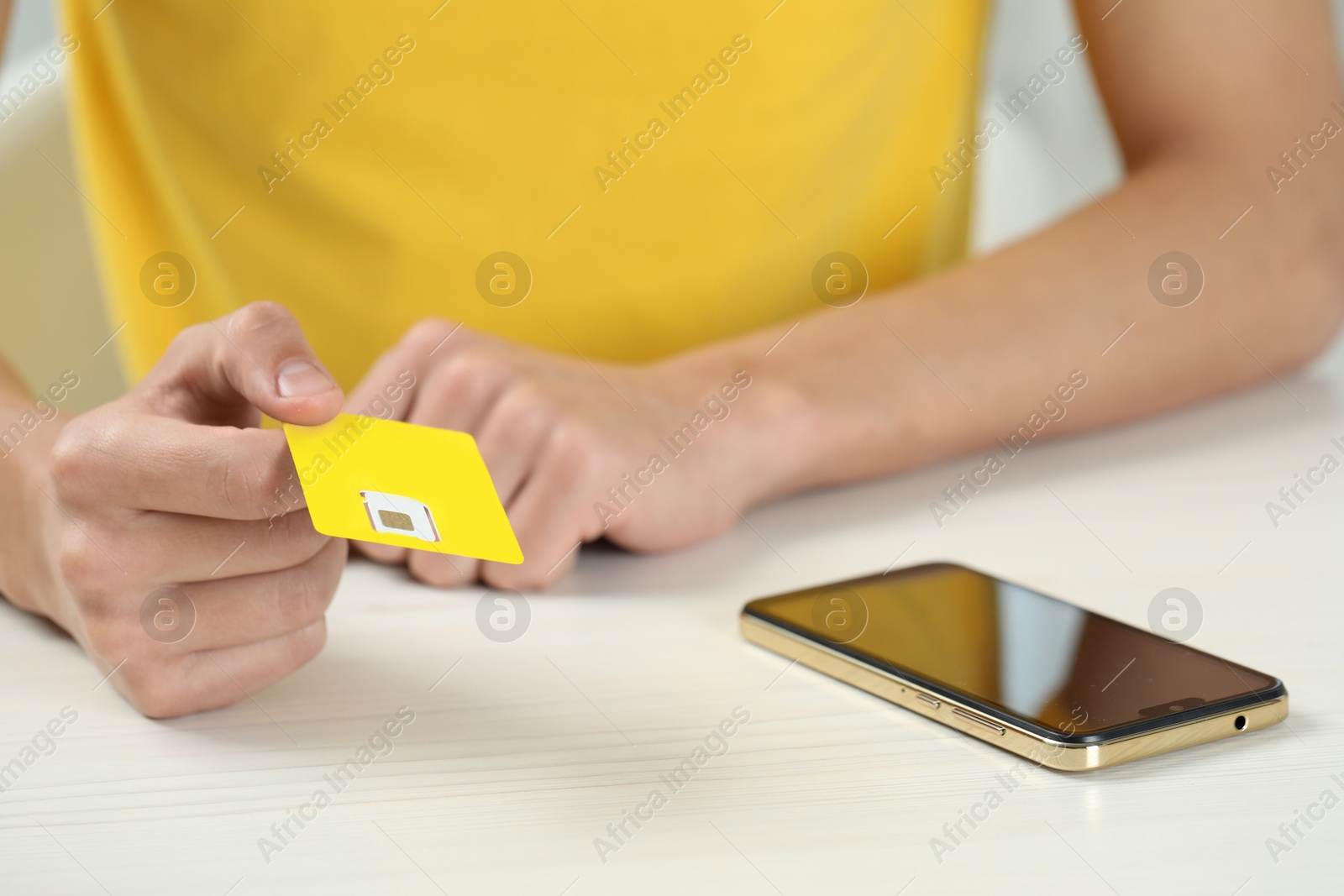 Photo of Man holding SIM card near smartphone at white wooden table indoors, closeup