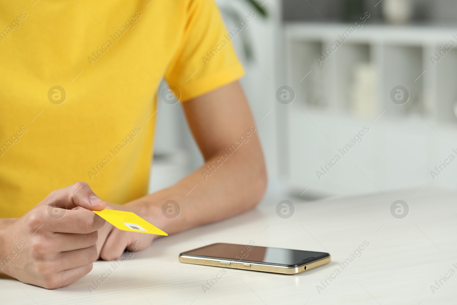 Photo of Man holding SIM card near smartphone at white wooden table indoors, closeup. Space for text