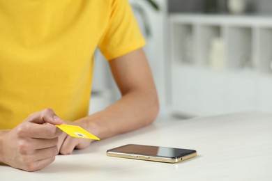 Photo of Man holding SIM card near smartphone at white wooden table indoors, closeup. Space for text