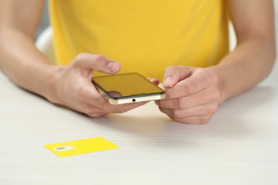 Man with ejector opening SIM card tray in smartphone at white wooden table, closeup