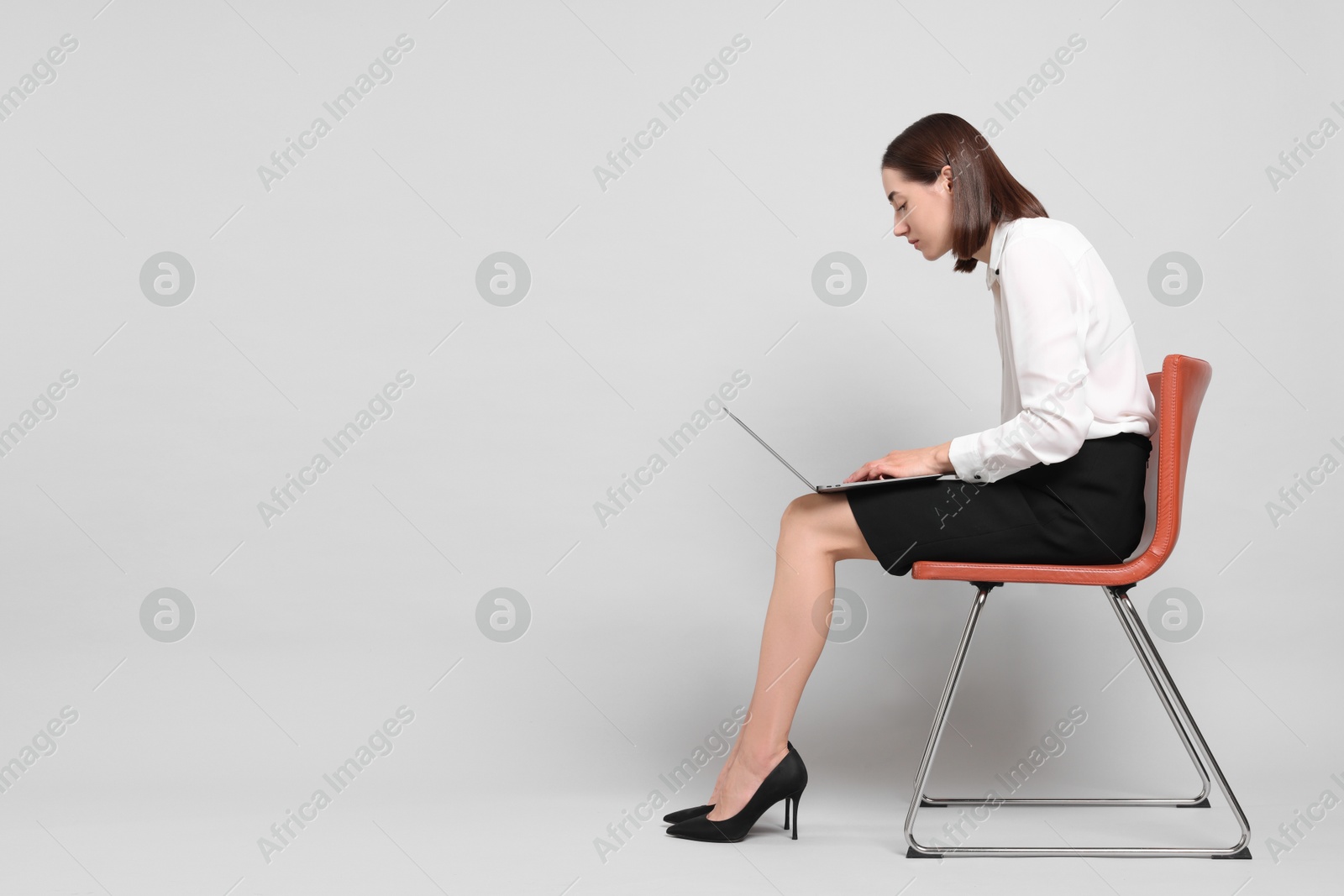 Photo of Woman with poor posture sitting on chair and using laptop against gray background, space for text