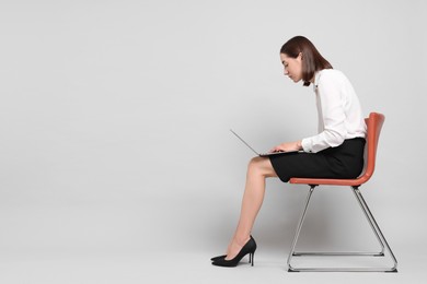 Woman with poor posture sitting on chair and using laptop against gray background, space for text