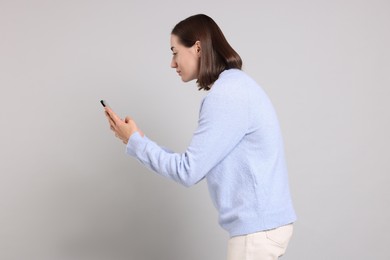 Woman with poor posture using smartphone on gray background